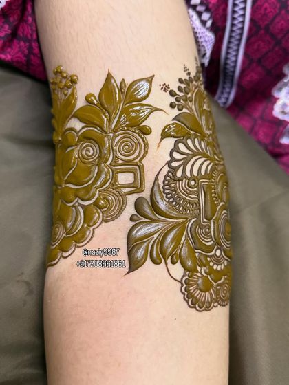 A close-up of a floral motif being created on the arm. The raised paste shows the precision of the application.