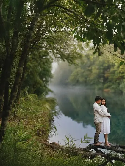 A quiet embrace while balancing on a fallen tree over a still, reflective river. The mist on the water and the lush greenery create a peaceful and deeply romantic atmosphere for this pre-wedding shot.