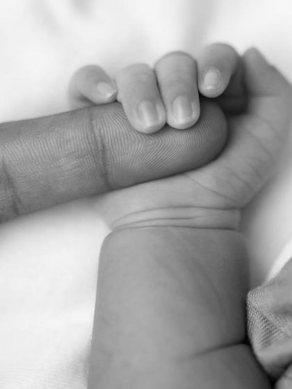 A close-up black and white photo of a newborn's hand tightly gripping an adult's finger, symbolizing trust and connection.