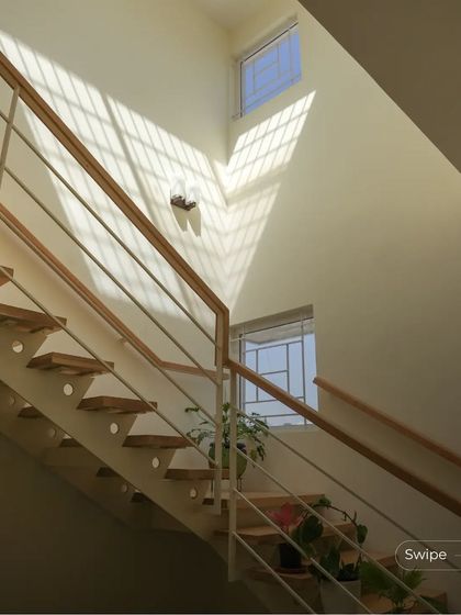 The sleek, modern staircase of the Anand Residence is bathed in natural light from a high window, making the space feel bright and airy.