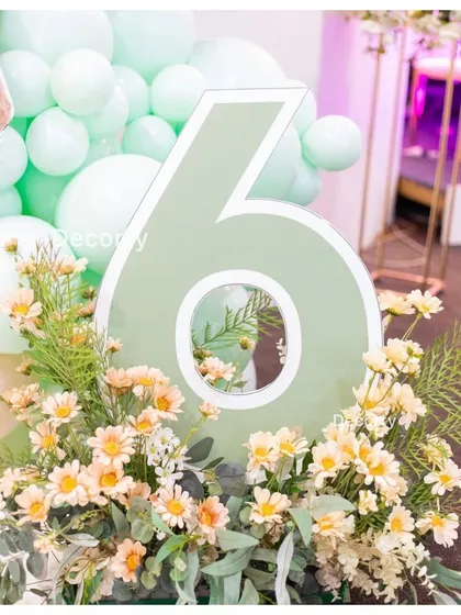 A stylish mirrored number '6' prop, surrounded by fresh flowers, for the Labubu party.