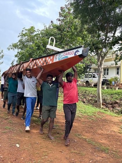 Teamwork in action as participants carry a large canoe to the water's edge, a fundamental part of camp life.