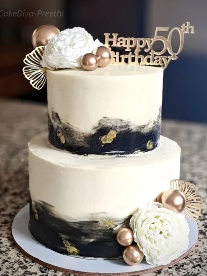 This modern, two-tier abstract cake was designed for a 50th birthday. The black-and-white buttercream design with gold leaf accents offers a sophisticated and artistic option for milestone celebrations.