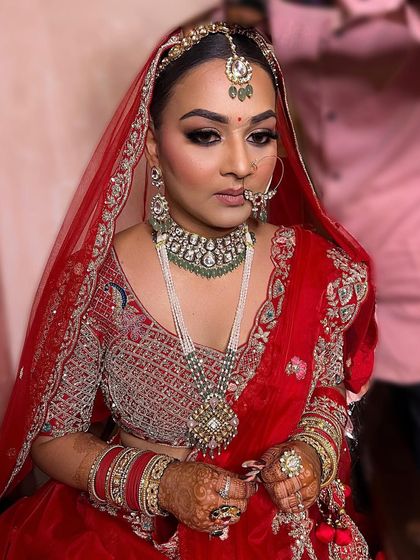 This full-shot showcases the complete royal bridal look. The makeup is designed to complement her red lehenga and heavy jewellery, creating a look of pure elegance.