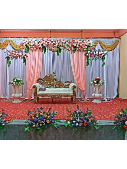 A classic stage decoration for a wedding reception or engagement. The combination of fresh flowers, elegant drapery, and traditional seating creates a timeless and beautiful backdrop for your special day.