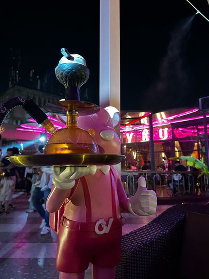 A quirky shot of a statue holding a hookah. This highlights the unique and playful decor of the bar.
