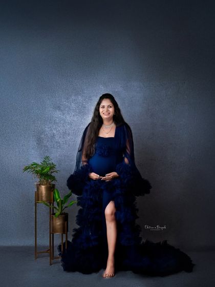 A full-length portrait in a stunning navy blue gown. The simple planters add a touch of green to this elegant and modern maternity look.