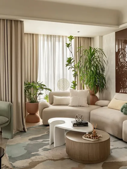 A cozy corner in the Kolkata home, featuring a plush beige sofa and layered coffee tables. The abstract rug introduces soft blues and greens, while large plants bring life and a natural element into the room.