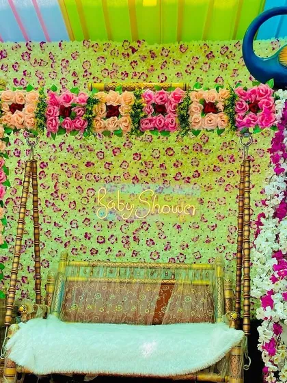 A traditional swing setup for a baby shower, decorated with flowers and placed against a floral backdrop with a peacock prop.