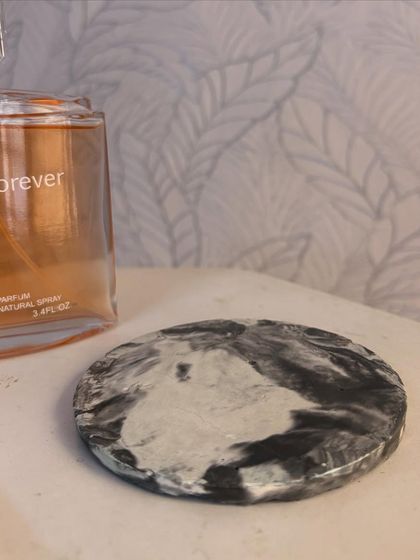 A simple, elegant shot of the marbled ceramic coaster next to a perfume bottle, showing its use as a stylish base for your vanity items.