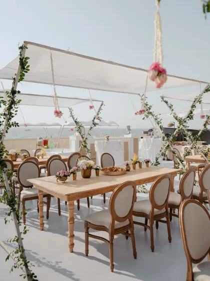 An elegant beachside lunch setup in Goa, with white canopies, climbing greenery, and rustic wooden tables, creating a chic and relaxed ambiance.