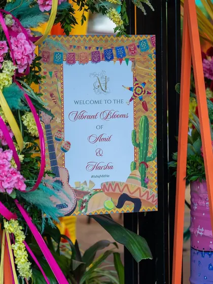 The welcome sign for the "Vibrant Blooms of Amit & Harsha" carnival, featuring a fun, illustrated design with guitars and cacti.
