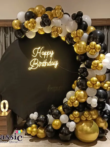 For milestone birthdays like a 60th, we design elegant setups. This one features a black and gold balloon semi-arch on a circular backdrop with a custom neon sign and marquee numbers.