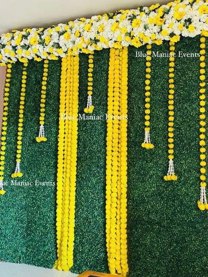A simple yet elegant Haldi/Mehendi backdrop with a green wall and hanging marigold and tuberose garlands.