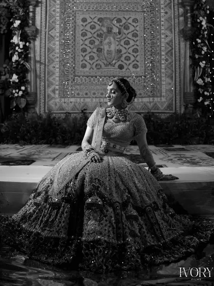 A stunning black and white portrait of the bride seated on the mandap. The intricate details of her lehenga are beautifully highlighted in this timeless shot.