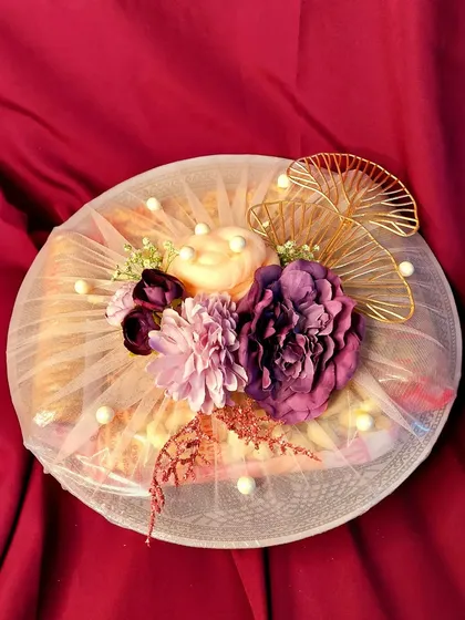 A beautifully decorated dry fruit platter for a wedding trousseau. The net wrapping, pearl details, and a large floral centerpiece make this a classic and elegant gift.
