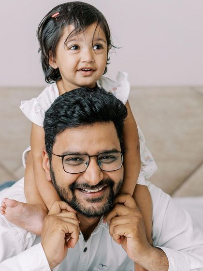 A father with his daughter on his shoulders, both smiling. A fun and playful moment captured indoors.