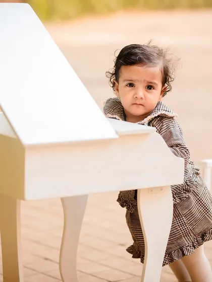 A curious baby girl peeking over the top of a miniature piano, a candid moment from her milestone session.