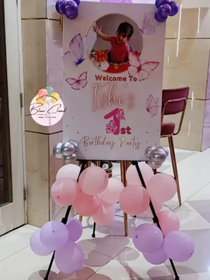 A personalized welcome easel sign for a first birthday party, decorated with pastel balloons.