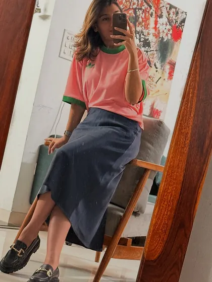 A trendy look with a pink t-shirt, midi skirt, and loafers, showing a more playful and modern style.