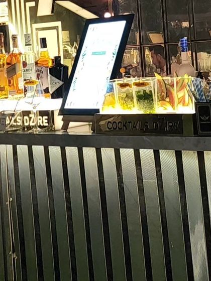 This bar setup features a digital menu and dedicated sections for different types of cocktails, like this gin bar with fresh herbs and garnishes, making it easy for guests to choose their drink.