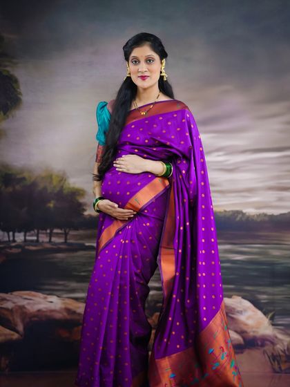 A simple and elegant solo portrait of the mother-to-be in her beautiful purple saree. Her hands gently rest on her baby bump, showcasing the maternal bond.