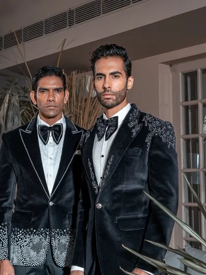 Our collection offers coordinated yet individual styles for grooms and groomsmen. Here, two distinct embellished velvet tuxedos are shown, one with shoulder embroidery and the other with crystal work on the lapel and cuffs, creating a unified and luxurious wedding party aesthetic.