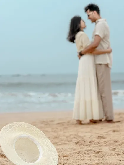 A beautifully composed shot focusing on a simple detail, a hat on the sand, with the couple sharing a moment in the background. This storytelling approach adds depth and a sense of place to your pre-wedding album.