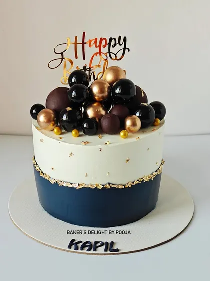 Elegance in every layer. This navy blue and white cake is adorned with faux chocolate balls in navy, black, and gold, with a touch of gold leaf for a classy birthday celebration.