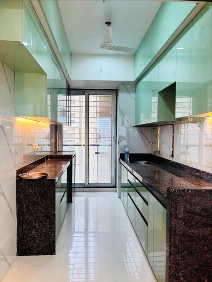 A full view of a sleek parallel kitchen layout in Ghansoli, Navi Mumbai. The high-gloss mint green cabinets reflect light beautifully, making the space feel open and bright, while the dark granite countertops provide a durable work surface.