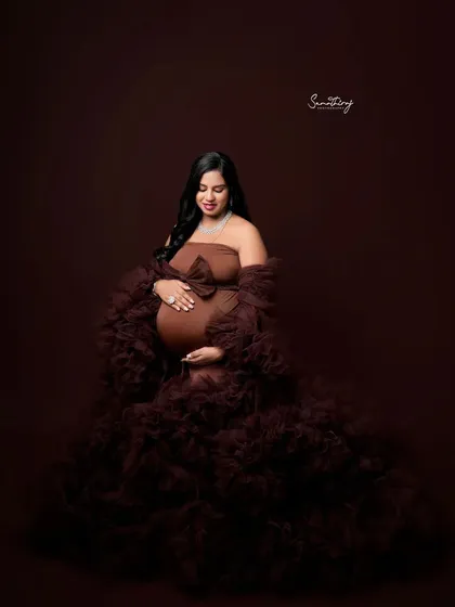 A stunning solo portrait of a mother-to-be in a rich brown gown with a large bow. The dramatic ruffled train and the deep color create a luxurious and high-fashion look.