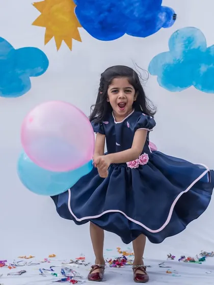Twirling into the party with a heart full of joy. This navy blue dress has a full skirt with pink trim that’s made for spinning, and the floral details add a sweet, feminine touch.