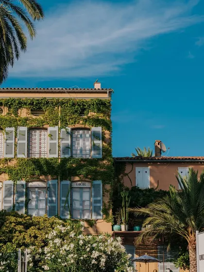 An ivy-covered building with classic blue shutters in St. Tropez, likely the Dior restaurant. It's a perfect example of the town's chic, picturesque scenery.
