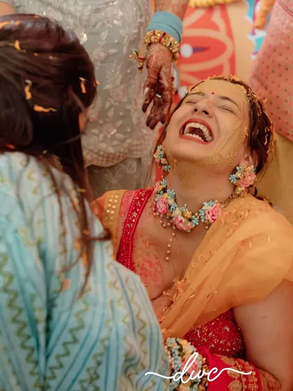 A candid shot of pure joy during a Haldi ceremony, with the bride bursting into laughter as she's covered in turmeric by her loved ones.