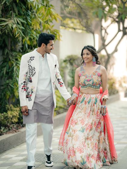 A happy, candid shot of a couple walking together, dressed in vibrant floral outfits perfect for a Haldi or Mehendi ceremony. Their smiles capture the joy of the occasion.