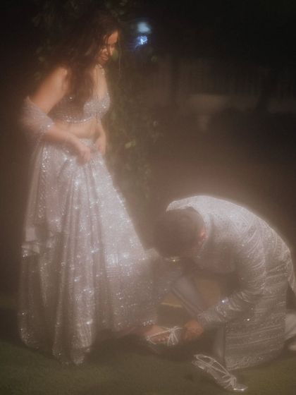 A modern-day fairytale moment. The groom helps his bride with her shoe, a gesture of love and care captured in a dreamy, soft light.