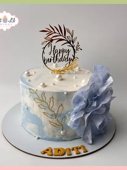 A beautiful birthday cake for Aditi, with a blue watercolor effect, hand-painted gold leaves, and a delicate wafer paper flower.