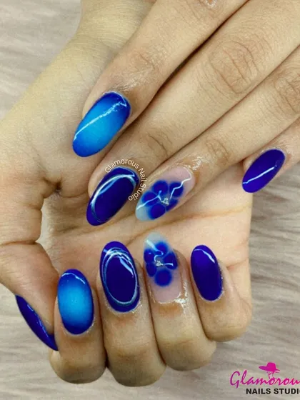 We treat every nail like a tiny canvas. This design showcases our skill in creating detailed floral art, featuring deep blue ombre effects and delicate, hand-painted flowers on almond-shaped extensions.
