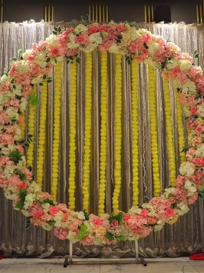 A beautiful circular backdrop made of pink and white flowers with strings of yellow marigolds. This versatile design is perfect for a Haldi, Mehandi, or Sangeet photo booth.