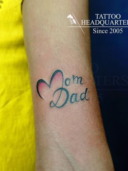 A "Mom Dad" tattoo where the words are connected by a heart, a classic symbol of love for one's parents.