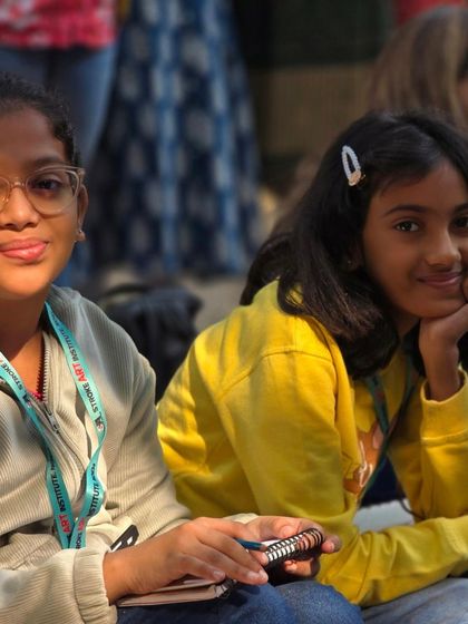 Two young students enjoying the outdoor art session, taking a moment to watch a demonstration and soak in the creative atmosphere.