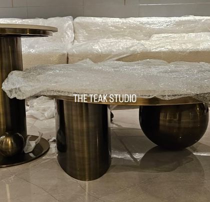 A set of modern coffee tables ready for delivery. This pairing includes a taller, cylindrical side table and a lower, globe-base coffee table, both with a metal finish and stone tops.
