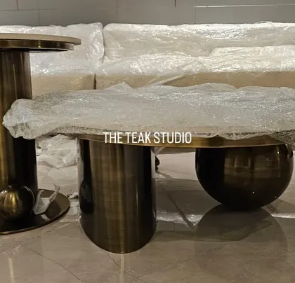 A set of modern coffee tables ready for delivery. This pairing includes a taller, cylindrical side table and a lower, globe-base coffee table, both with a metal finish and stone tops.