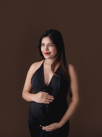 A classic portrait of a mom-to-be in a black halter dress against a simple studio background.