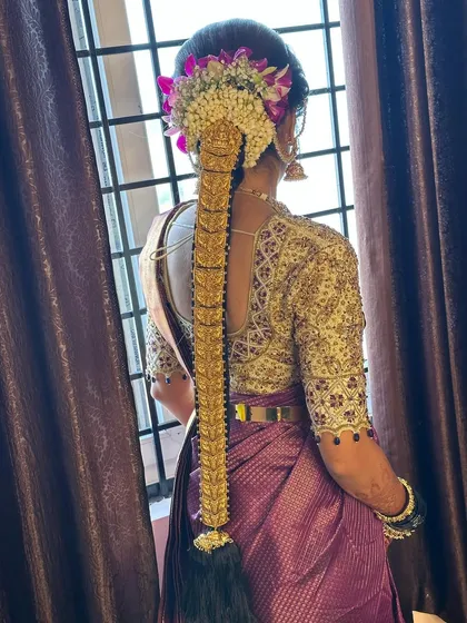 This bride's Muhurtham braid is decorated with a full set of gold temple jewellery and accented with fresh orchids. The purple flowers add a unique touch to the traditional hairstyle.