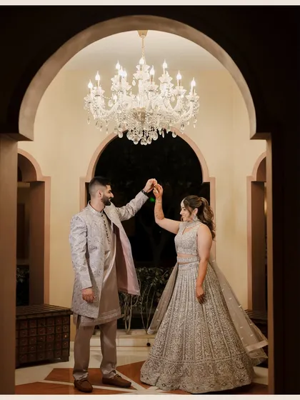 A romantic moment under a grand chandelier, as the groom twirls his bride during their engagement or Sangeet ceremony.
