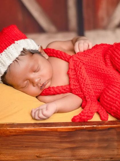A closer view of the 'Santa' theme, showing the baby nestled in a tiny wooden bed. The details, like the small wrapped gifts, complete the festive scene.