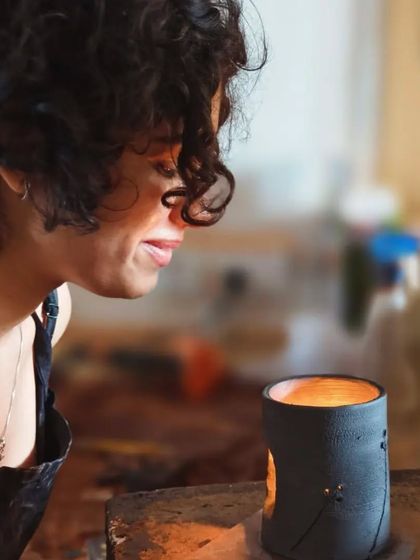 The joy of seeing your creation complete. A student smiles as she looks at her finished candle holder, the warm light glowing through the patterns she carved.