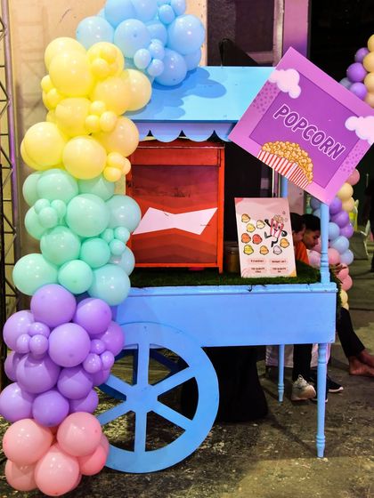 A bright and cheerful popcorn cart decorated with a rainbow balloon garland, adding to the festive atmosphere.
