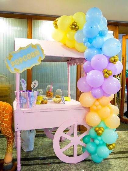 A charming pink popcorn cart decorated with a pastel balloon garland, serving up a classic carnival treat.
